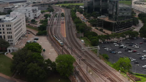 Aerial-view-of-train-driving-on-track.-Forwards-tracking-footage-of-metropolitan-passenger-DART-Light-Rail-approaching-to-station.-Dallas,-Texas,-US