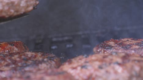 chef quickly flipping burger with fire flames and smoke rising on barbecue. minced steak meat traditionally put in bun. delicious unhealthy summer outdoor food.