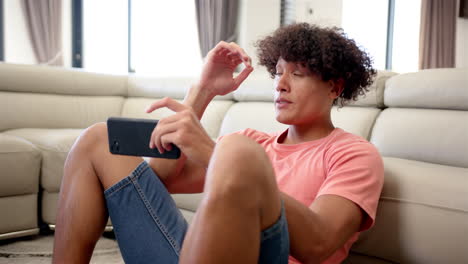 un joven biracial molesto y estresado con el cabello rizado está sentado, sosteniendo un teléfono inteligente