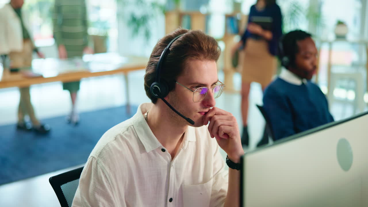 A man wearing a headset and glasses is talking on the phone in an office setting.