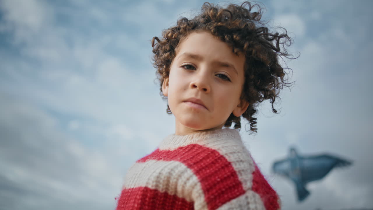 Portrait curly little boy at cloudy sky. Dreamy child resting autumn shore