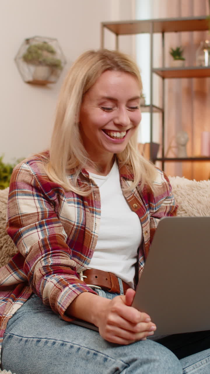 Adult woman raising hands in victory at home celebrating happy online success game win on laptop