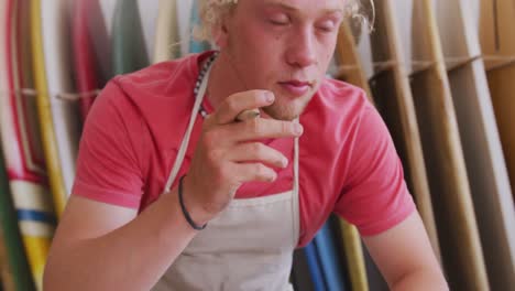 caucasian male surfboard maker working in his studio and making a wooden surfboard