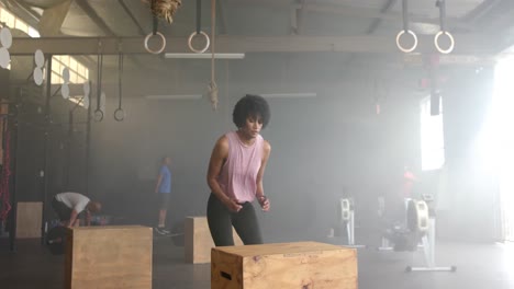 focused african american woman jumping on and off box, cross training at gym, in slow motion