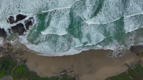 top down view over ocean waves with foam splashing on the seashore - drone shot