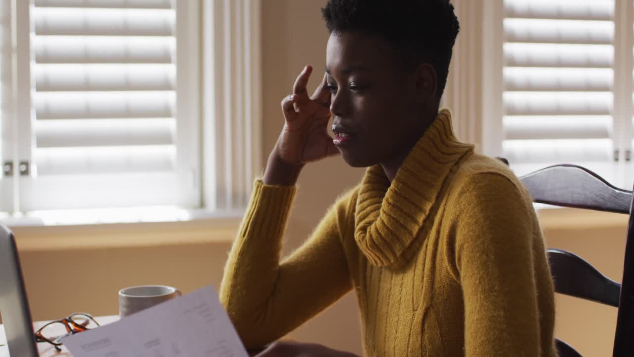 Stressed african american woman holding a document while working from home