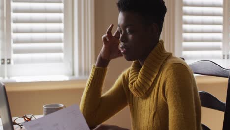 mujer afroamericana estresada sosteniendo un documento mientras trabaja desde casa