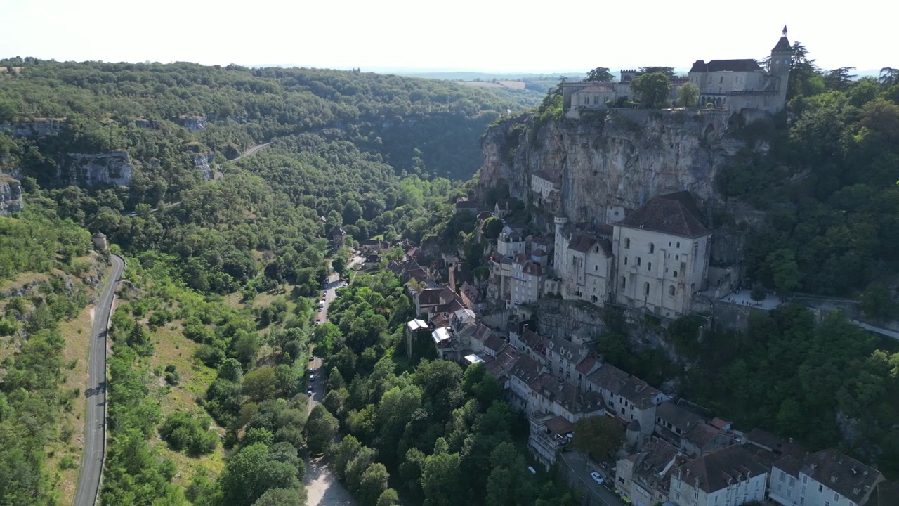 Veduta aerea con drone di una piccola e antica città medievale nella campagna francese, situata su una rupe rocciosa con un castello e una cattedrale, circondata da una verde foresta montana a Rocamadour.