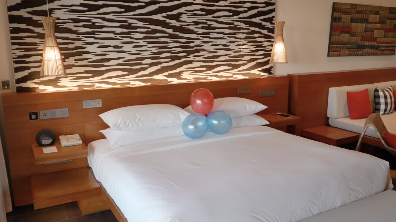 Ballondecoratie boven een bed met puur wit linnen beddengoed in een hotelkamer. Opname met pan naar rechts
