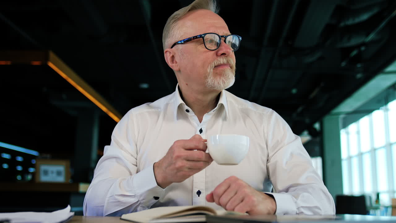 Calm relaxed Caucasian man sits in office with a cup in hands. Low angle view on the businessman at coffee break.