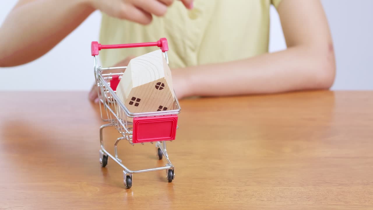 A person imagines their future home while playfully placing a miniature house a shopping cart