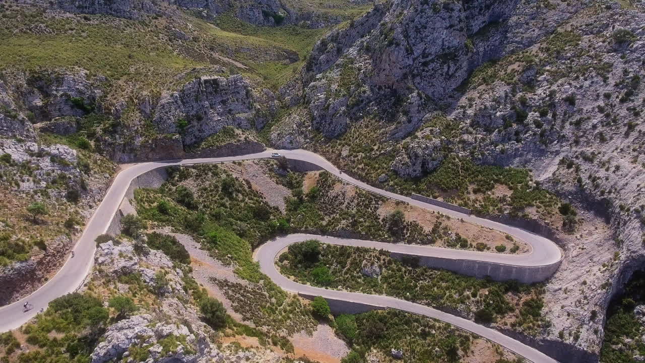 Letecký pohled směřující k klikaté horské silnici na Mallorce, po které jezdí cyklisté i auta