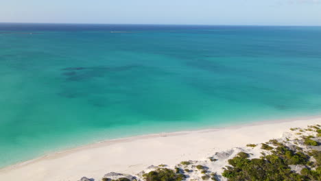 romantic couple walking on white sand beach surrounded by turquoise blue sea in turks and caicos islands. aerial drone orbit (pull-away)