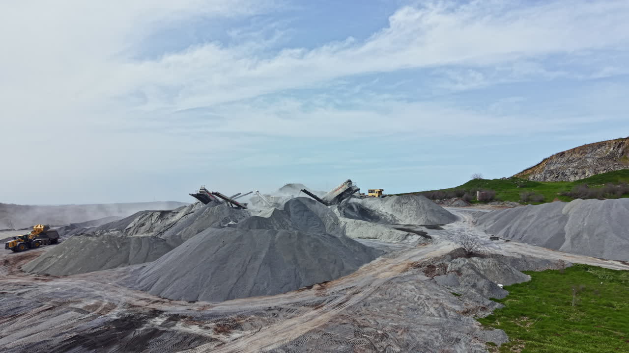 Tambang granit beroperasi dengan tumpukan batu besar dan mesin bekerja di bawah langit berawan pada siang hari.