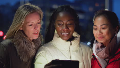 group of female friends on city street at night ordering taxi using mobile phone app