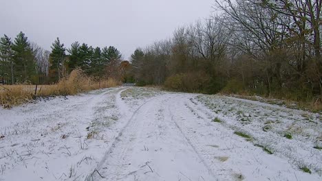 POV from an off road vehicle ATV while driving on a snow covered trail through a grassy field and into the woods on an early winter afternoon; point of view