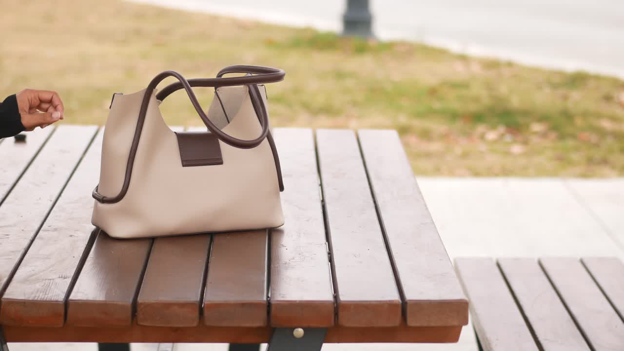 bolso de mano beige de la mujer en la mesa de picnic de madera