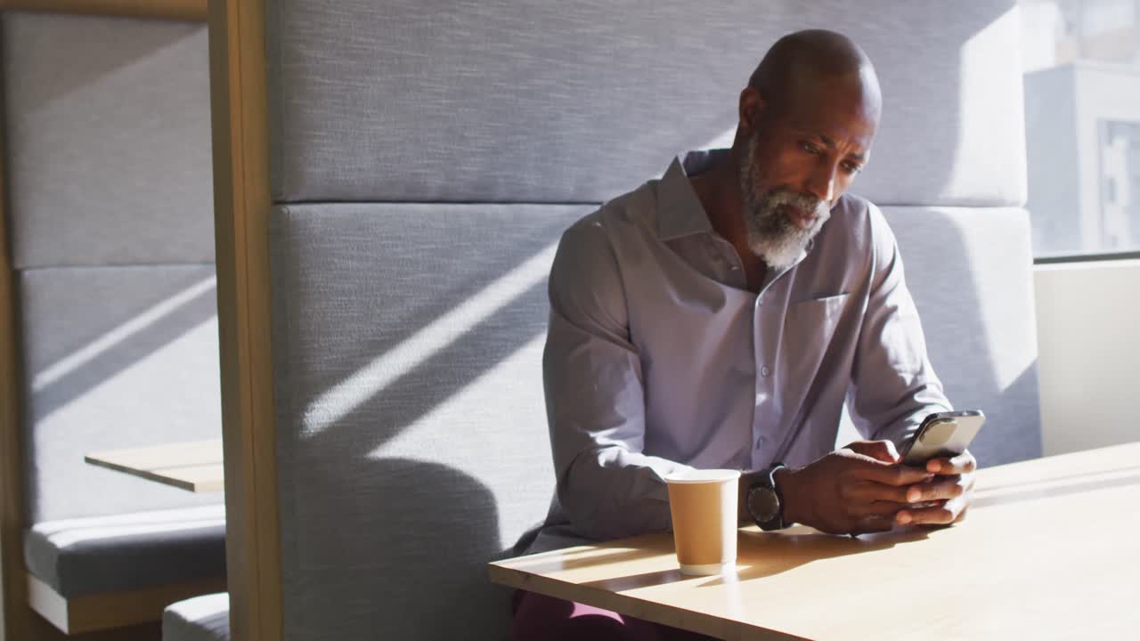 African american businessman sitting at table and using smartphone at office