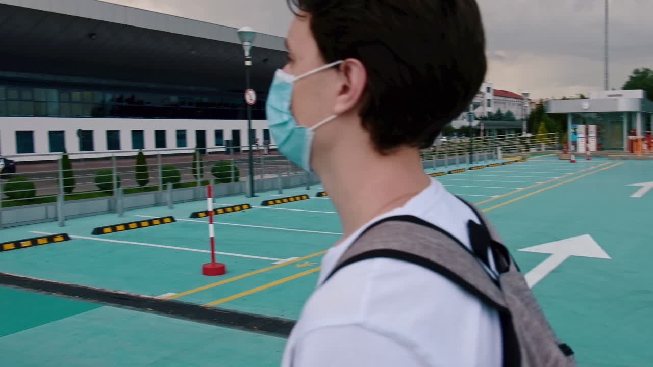CHISINAU, MOLDOVA - JUNE 19, 2020: Young man in white t-shirt, backpack and surgical mask walking to the airport. Traveling during Corona Virus pandemic outbreak