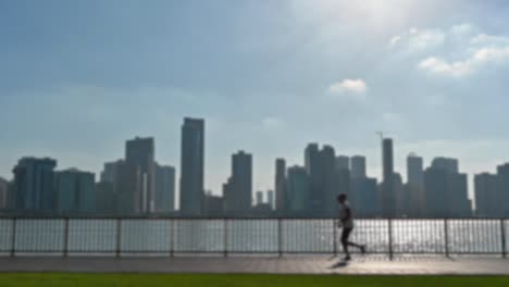 Cámara-Lenta,-Fuera-De-Foco:-Un-Joven-Haciendo-Ejercicio-Al-Aire-Libre-Con-Una-Vista-De-La-Ciudad-En-El-Fondo-Del-Lago-Khalid-En-Sharjah,-Emiratos-árabes-Unidos