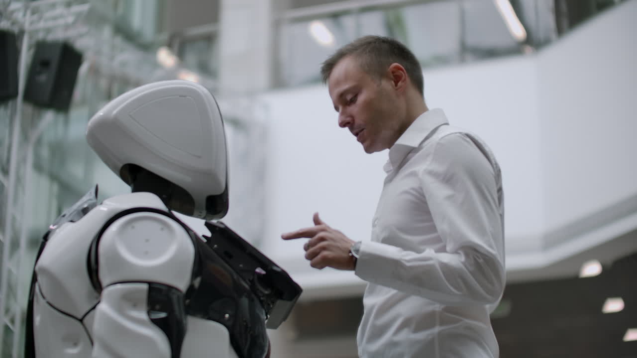 un hombre se para con un robot bot y le hace preguntas y pide ayuda haciendo clic en la pantalla en el cuerpo del robot. la interacción humano-robot en el mundo moderno