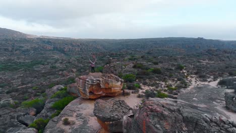 Man-standing-on-rock-formation-with-his-arms-spread-4k