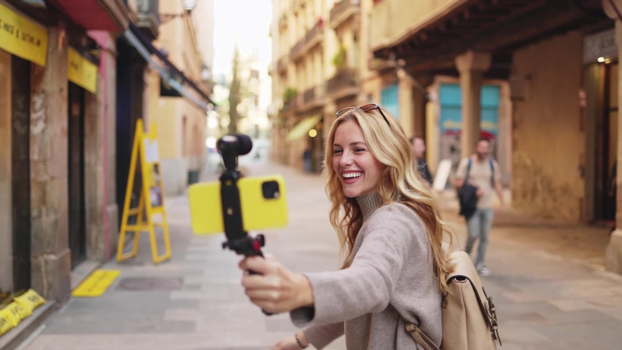 Donna bionda allegra che fa vlogging con lo smartphone in una strada urbana