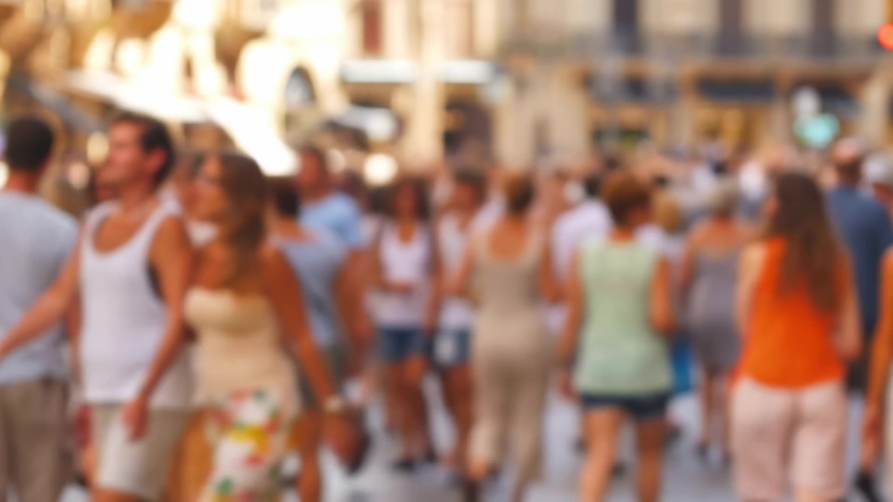 Scena a fuoco morbido di molte persone che camminano per una luminosa strada urbana, suggerendo il pendolarismo quotidiano, l'attività pubblica e la vita cittadina energica alla calda luce del giorno.