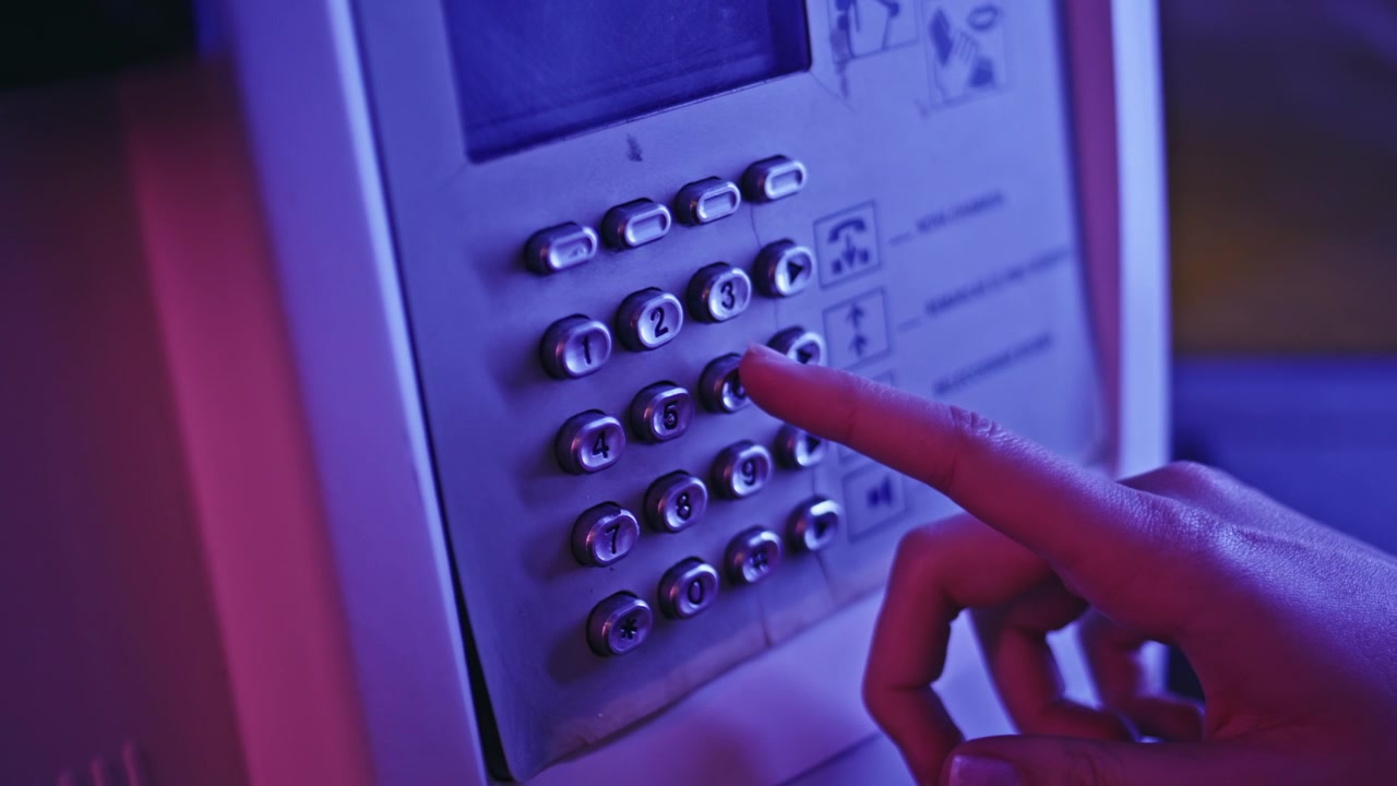 Primo piano di una mano che compone un numero sulla tastiera di un telefono pubblico. Cabina telefonica illuminata al neon, chiamata notturna