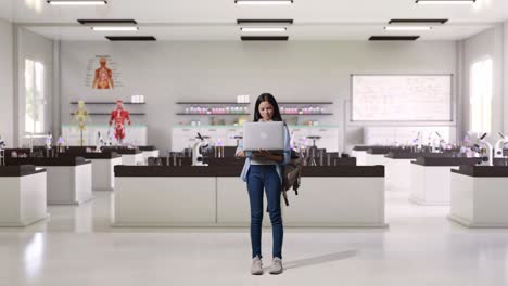 cuerpo lleno de estudiante adolescente asiática con una mochila sonriendo y escribiendo en una computadora portátil mientras estaba de pie en el laboratorio de ciencias