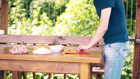 travelling the guy is cooking pilaf it is in a summer house cuts carrots there is a plate with pieces of meat on the table