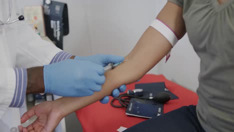 diverse male doctor and female patient taking blood sample in consulting room, slow motion