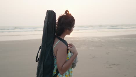 embracing the coastal serenity, a young indian woman, adorned with her guitar secured on her back with a cover, finds harmony between music and the tranquil beauty of the beach