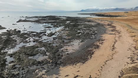 Aerial-view-of-rock-beach,-calm-sunny-day-in-Icelandic-Snæfellsnes-peninsula,-glacier-in-the-background