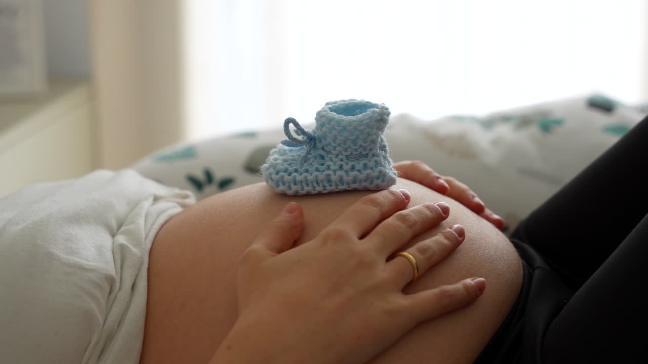 Stivaletti azzurri da neonato sul pancione di una donna incinta. Primo piano.