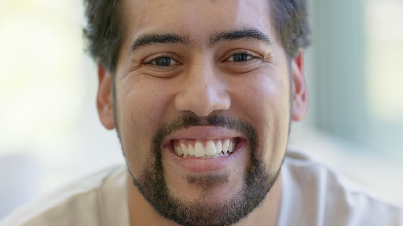 African American man gazing at camera, shifting to laughing with teeth visible, beard, light shirt