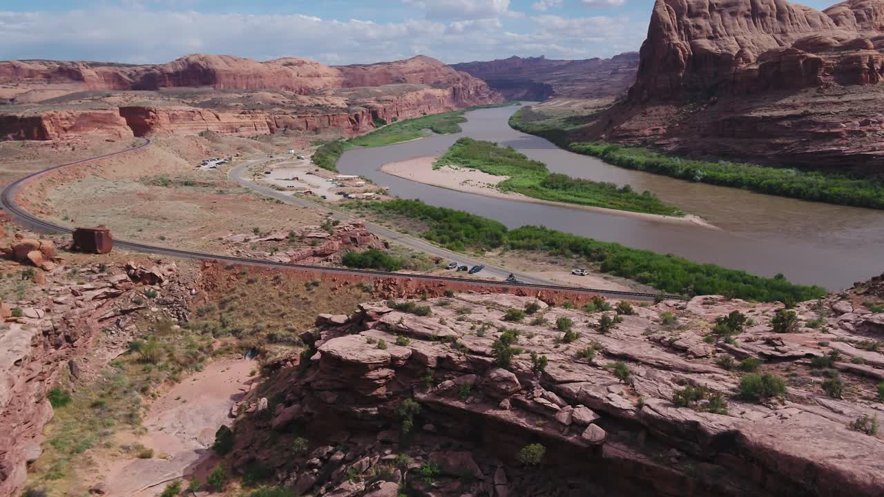 una toma de drone de 4k de acantilados escarpados y una vía ferroviaria que corre a lo largo del río colorado, cortando a través del paisaje único y accidentado del desierto cerca de moab, utah