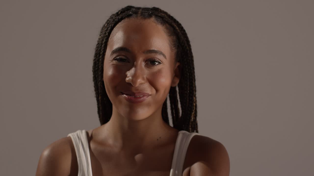 fotografía de belleza en el estudio de una mujer joven sonriente con el pelo largo trenzado contra un fondo neutral 1