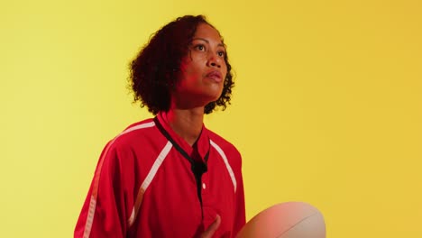 african american female rugby player with rugby ball over neon yellow lighting