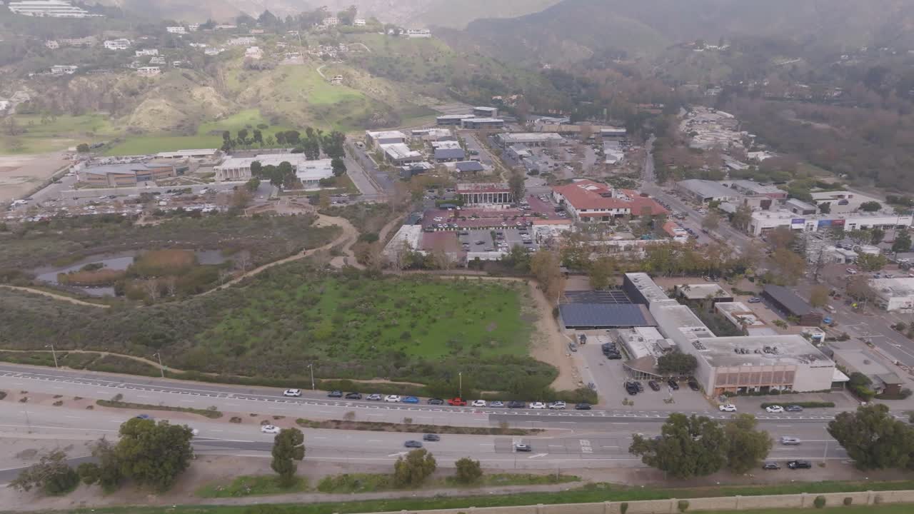 Sweeping aerial view capturing Malibu's cityscape and Highway 1 as it winds along the Pacific Coast, showcasing buildings, roads, and the coastal landscape from above