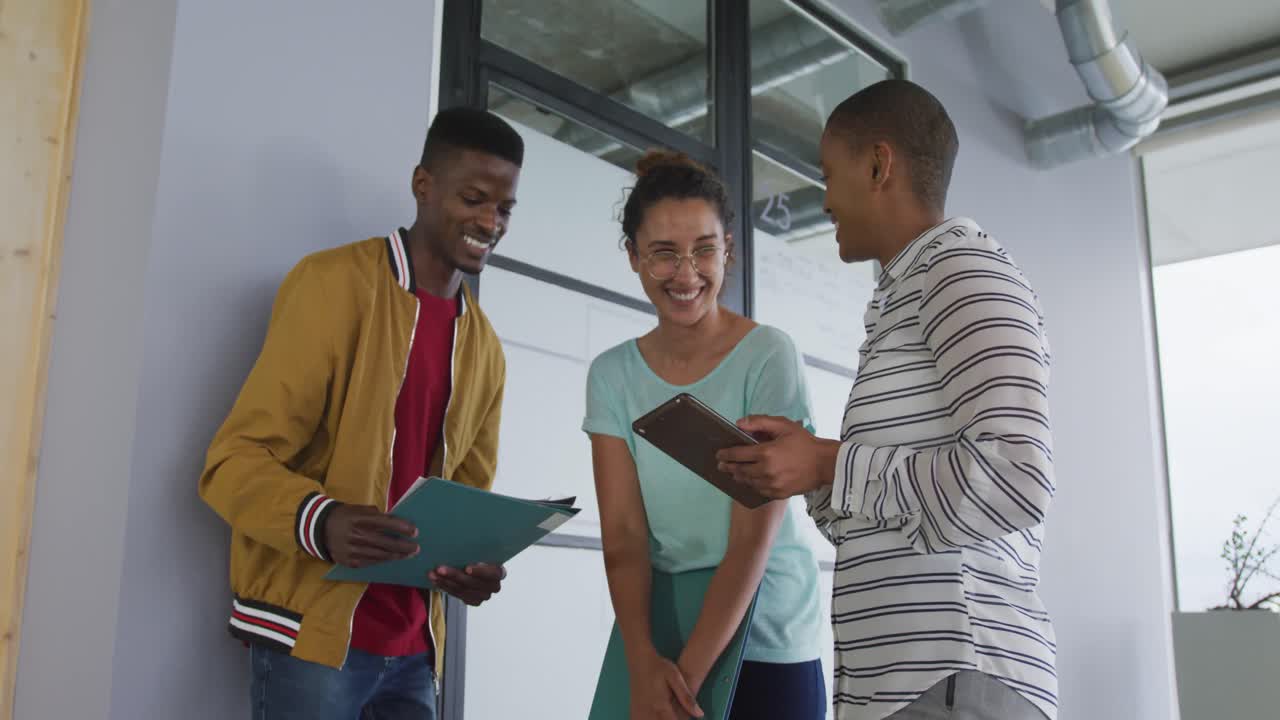 Smiling diverse male and female creative colleagues in discussion, looking at documents and tablet