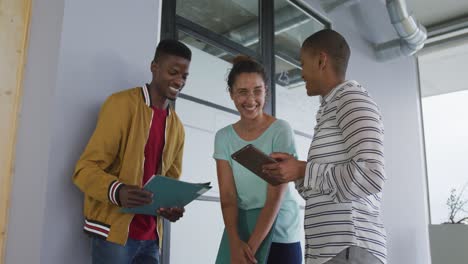 Smiling-diverse-male-and-female-creative-colleagues-in-discussion,-looking-at-documents-and-tablet