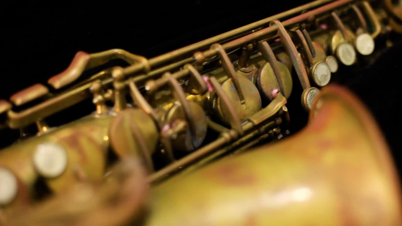 Dolly shot of a very old rusty alto saxophone with black background