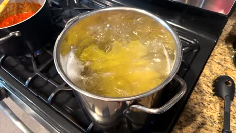 Looking-down-over-steaming-bubbling-stainless-steel-pot-of-pasta-cooking-slow-motion-on-kitchen-stove