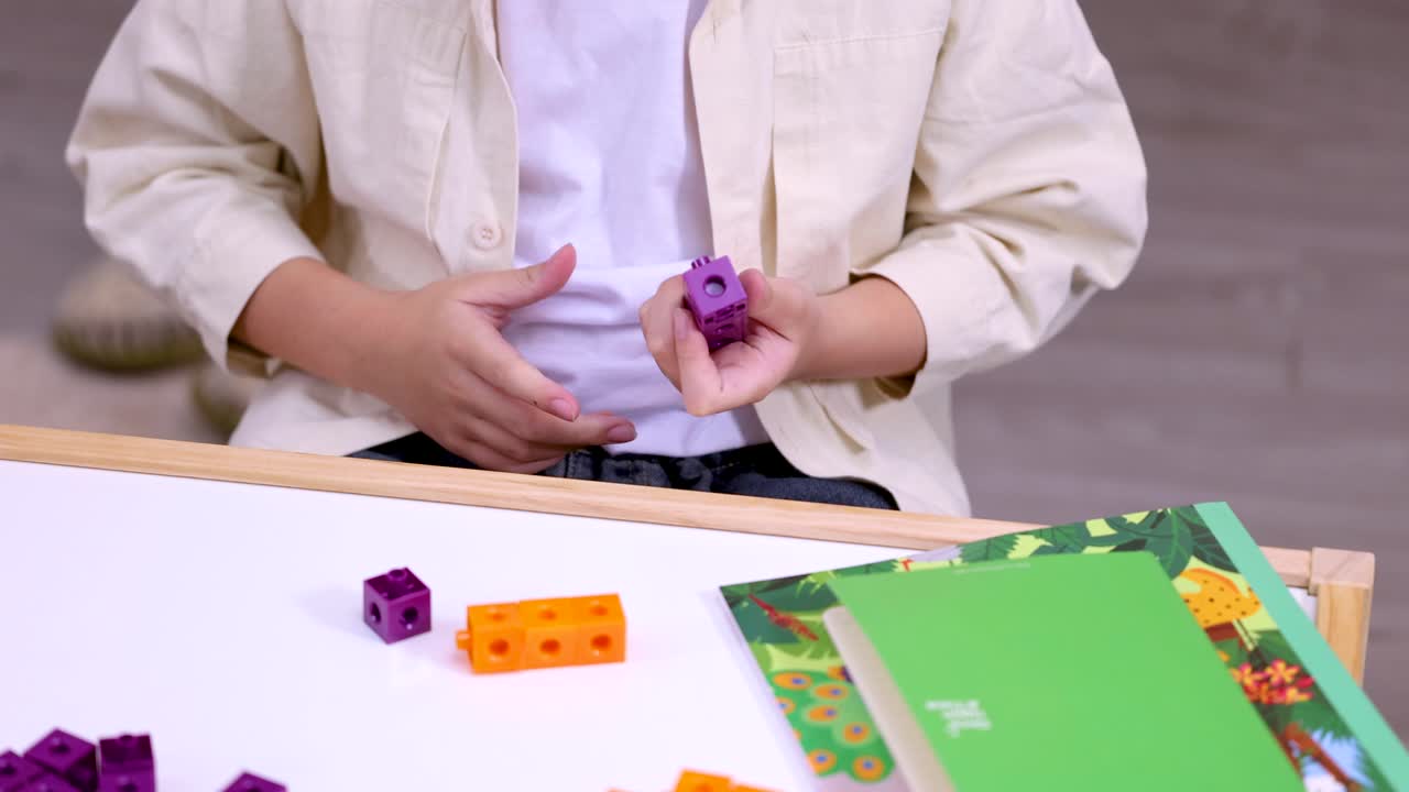 Close-up of child connecting colorful counting cubes on classroom desk with steady overhead framing