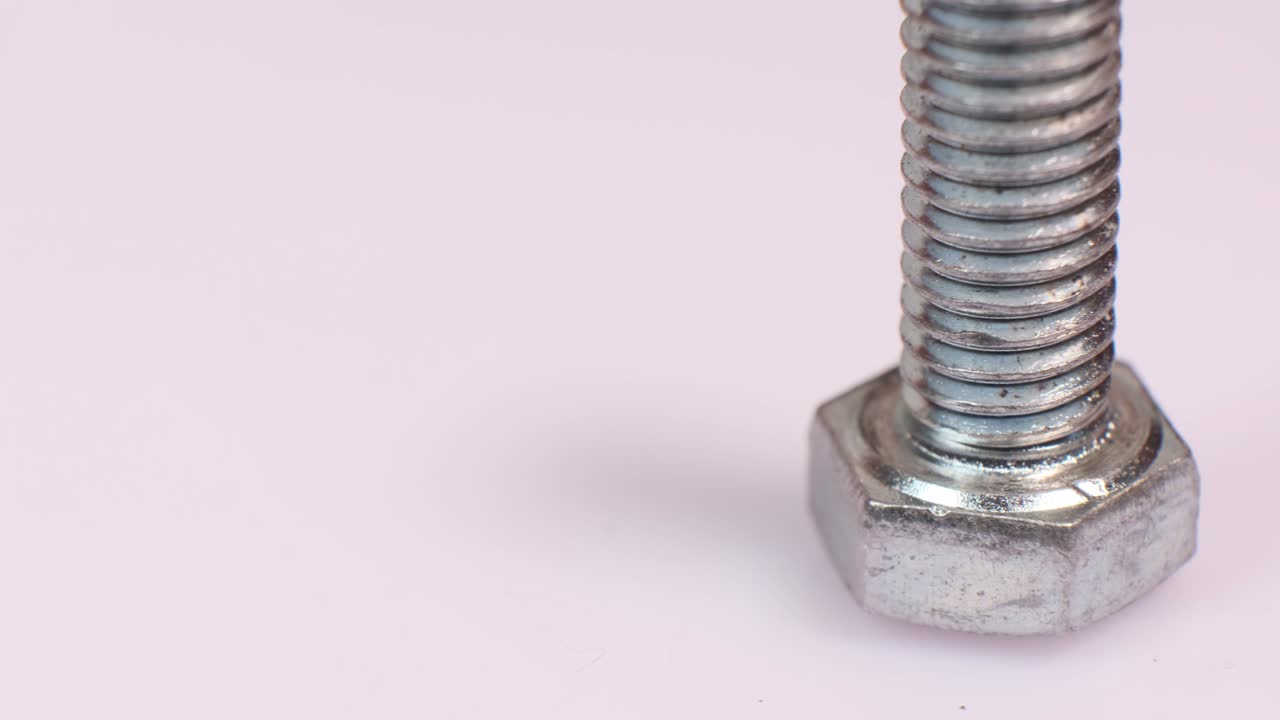 Rotating galvanized metallic screw close-up. Stainless steel bolt isolated on white background. Copy space.