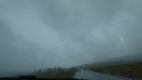 Rain-falling-on-the-car-window-during-a-downpour,-windshield-wipers-on