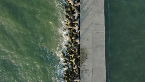 aerial establishing view of port of liepaja concrete pier, baltic sea coastline , sunny day summer evening, golden hour light, big waves splashing, wide birdseye drone shot moving forward