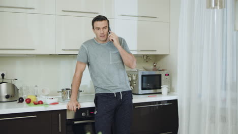 Angry-man-talking-phone-at-kitchen.-Aggressive-man-swinging-arms
