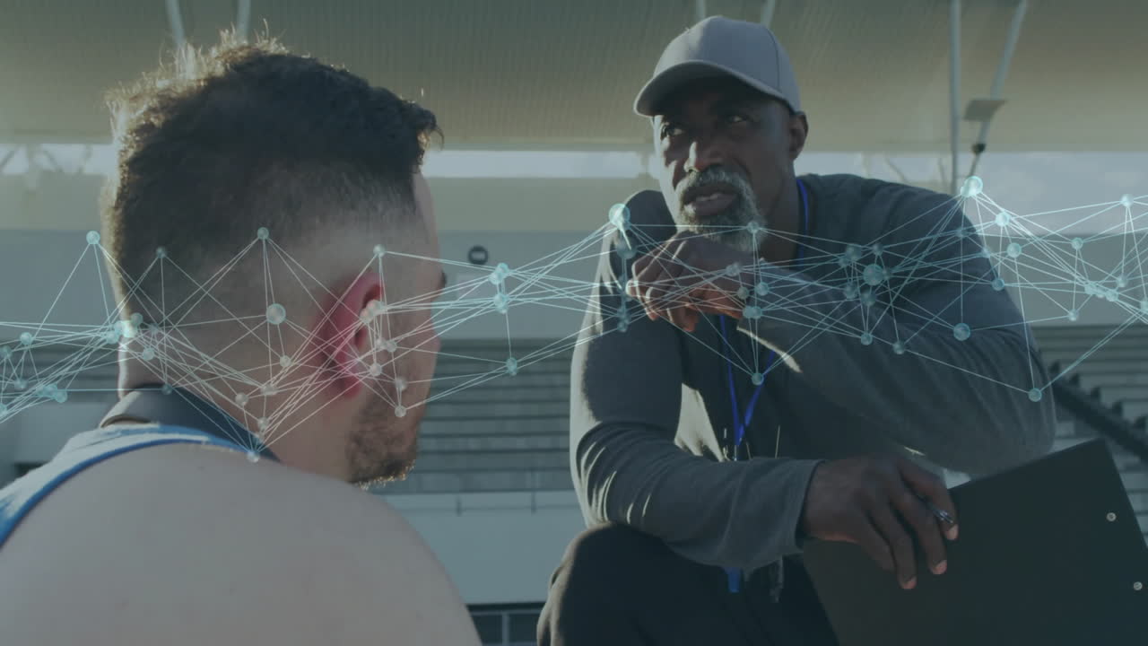 male coach pointing at clipboard in stadium with animated network overlay showing training data